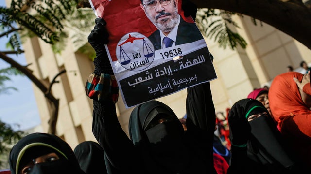  Supporters of Egypt's ousted President Mohammed Morsi holds an old presidential campaign poster of him with Arabic that reads, "Mohammed Morsi, president for Egypt, 2012, resurrection is the will of the people," during a protest a day before the trial of 