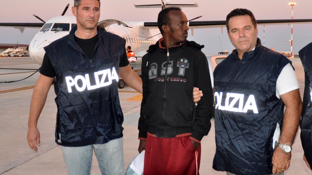 Two Italian policemen hold Somali national Mouhamud Elmi Muhidin upon his arrival to Palermo airport from the island of Lampedusa 