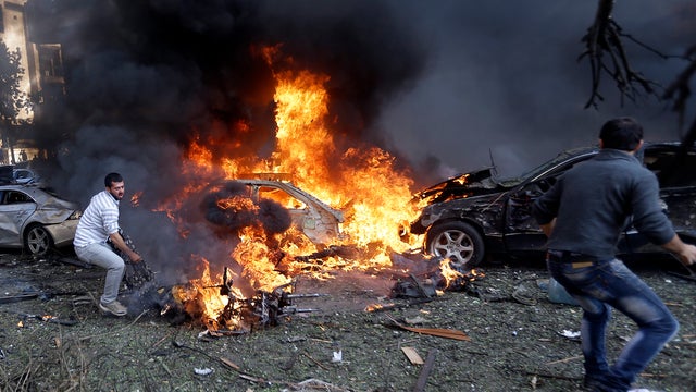 Lebanese men run to remove dead bodies from burned cars, at the scene where two explosions struck near the Iranian Embassy in Beirut 