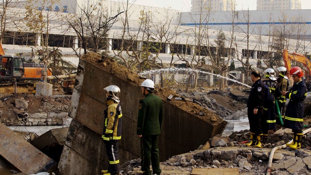 Policemen and firefighters check on a damaged site following a pipeline explosion in Qingdao in east China's Shandong province 