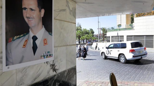 A poster of Syrian President Bashar al-Assad adorns a wall as a United Nations vehicle carrying inspectors from the Organisation for the Prohibition of Chemical Weapons (OPCW) leaves a hotel in Damascus 