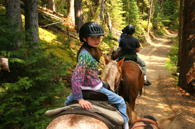 Young girl horse back riding on forest trail. 