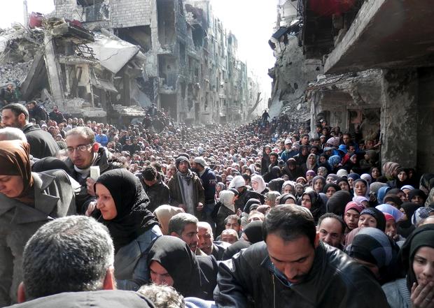 Palestinian residents of the Yarmouk camp in Damascus, Syria, queue for food aid 