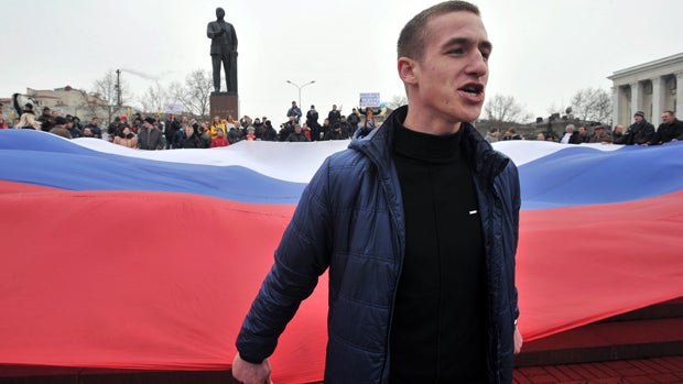 A pro-Russian activist holds part of a giant Russian flag near a statue of Lenin during a rally in Simferopol, the administrative center of Crimea, March 1, 2014. 