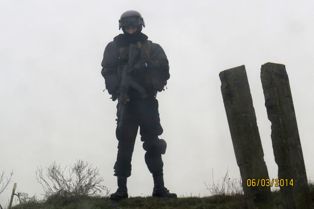 An unidentified armed man looks down from a hillop at a checkpoint on the Crimean border 