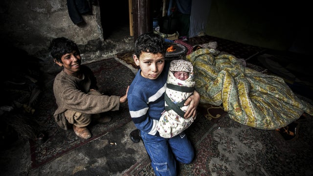 A Syrian refugee boy poses with his newborn brother as their mother lies near them in a house in the Basaksehir district of Istanbul 