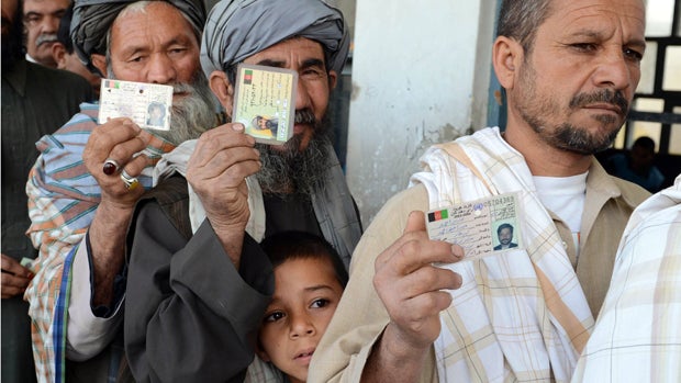 A young Afghan child stands among voters showing their national identity cards while they lineup before casting their votes at a local polling station in Kandahar, Afghanistan, April 5, 2014. 