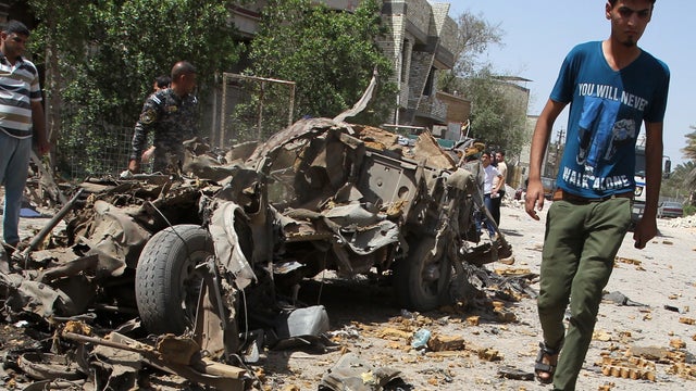 An Iraqi youth walks past the remains of a vehicle at the site of an explosion in Baghdad 