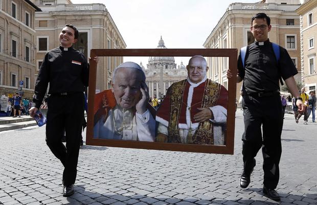 Two priest walk carrying pictures of Pope John Paul II (L) and Pope John XXIII in front of St. Peter's square 