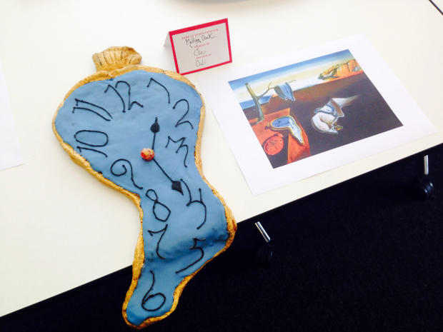 A cake inspired by Salvador Dali's "The Persistence of Memory" is seen next to a picture of the painting. 