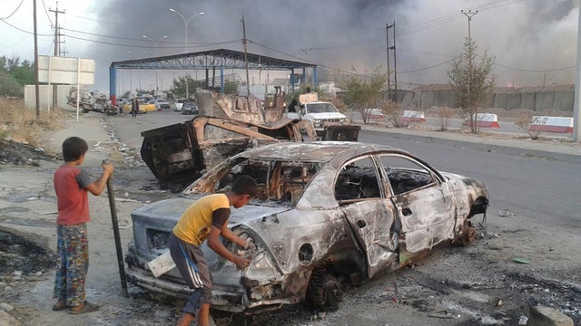 Civilian children stand next to a burnt vehicle during clashes between Iraqi security forces and Islamic State in Iraq and al Sham (ISIS) in the northern city of Mosul 
