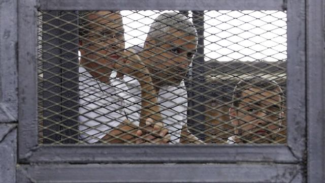 Al Jazeera journalists (L-R) Peter Greste, Mohammed Fahmy and Baher Mohamed stand behind bars at a court in Cairo 