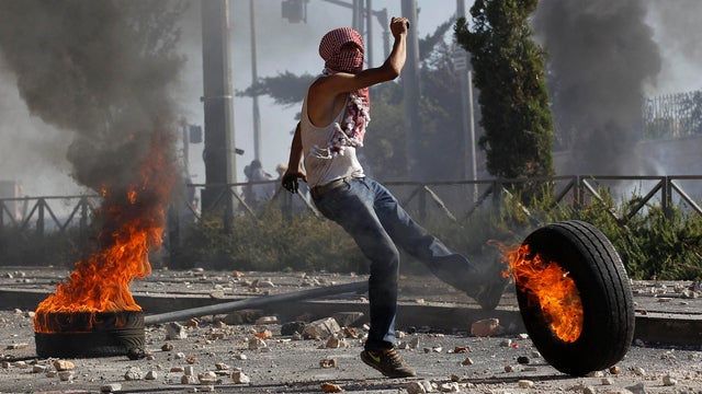 A Palestinian stone-thrower kicks a burning tire during clashes with Israeli police in Shuafat, an Arab suburb of Jerusalem, July 3, 2014. 