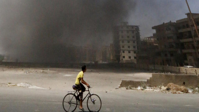 A man on a bicycle looks at smoke rising into the air after what activists say was shelling from forces loyal to Syria's President Bashar Assad in Raqqa 