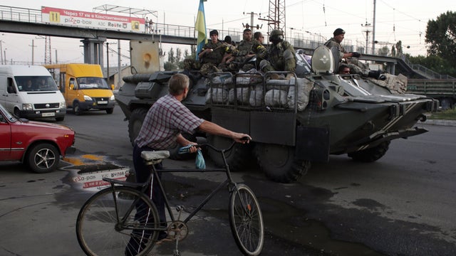 A cyclist watches a column of Ukrainian paratroopers stopped for a rest in Druzhkivka, Donetsk region 