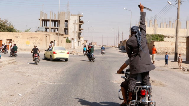Man holds up a knife as he rides on back of motorcycle touring streets of Tabqa city with others in celebration after ISIS militants took over Tabqa air base in northeast Syria , in nearby Raqqa city, on August 24, 2014 