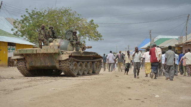 Residents walk along a street in Bulamareer next to AMISOM troops and a tank, in the Lower Shabelle region of Somalia 