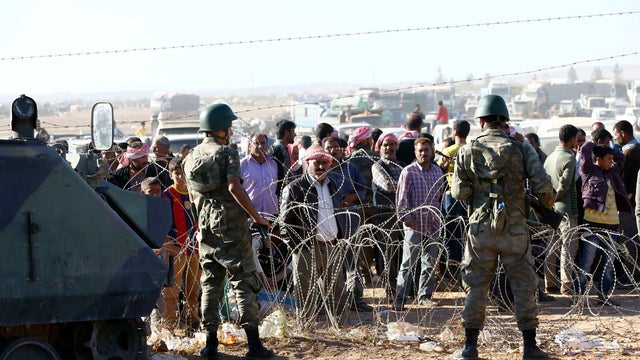 Turkish soldiers stand guard as Syrian Kurds wait behind a border fence near the southeastern town of Suruc  