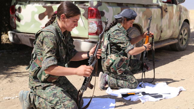 Two young female Kurdish fighters clean their weapons in a sheltered position, just a mile from ISIS militants, in the northern Syrian town of Mahmoodin 