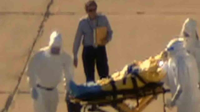 An unidentified man stands on the tarmac as workers in hazmat suits transfer Dallas nurse and Ebola patient Amber Vinson from an ambulance to a waiting plane 