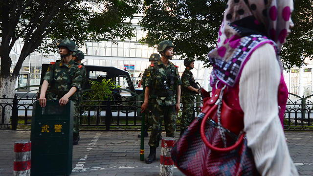 A Uighur woman walks past Chinese paramilitary police as they stand guard in the predominantly Muslim city of Urumqi 