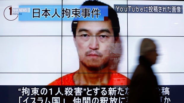 A man walks past screens displaying a television news program showing an image of Kenji Goto, one of two Japanese citizens taken captive by ISIS militants, on a street in Tokyo Jan. 25, 2015. 