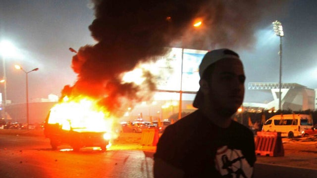 A soccer fan is seen near a police car, which was set on fire by fireworks, during clashes between soccer fans and security forces in front of a stadium on the outskirts of Cairo 