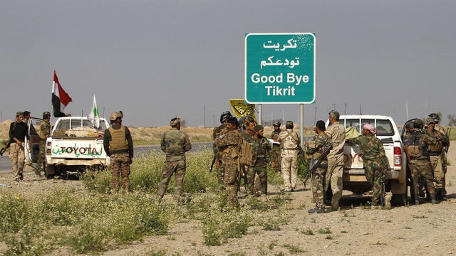 Shiite fighters gather with their weapons next to a sign in the town of al-Alam, just north of Tikrit 