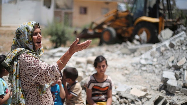 A Palestinian woman gestures as workers use a bulldozer to remove the ruins of buildings which were destroyed during the 50-day war between Israel and Hamas militants in the summer of 2014 