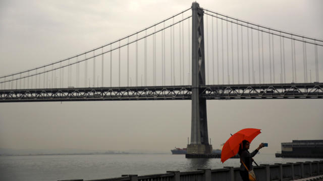 A woman takes a selfie beneath an umbrella near the San Francisco-Oakland Bay Bridge during a light rain in San Francisco, California, June 10, 2015. 