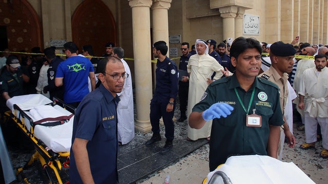 Kuwaiti emergency personnel pull stretchers past security forces outside the Shiite Al-Imam al-Sadeq mosque after it was targeted by a suicide bombing during Friday prayers in Kuwait City 