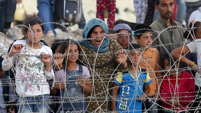 Syrian Kurds from Kobani wait behind the border fences to cross into Turkey as they are pictured from the Turkish border town of Suruc in Sanliurfa province, Turkey 