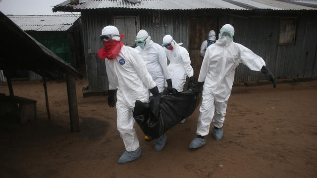 A Liberian burial team wearing protective clothing retrieves the body of a 60-year-old Ebola victim from his home 