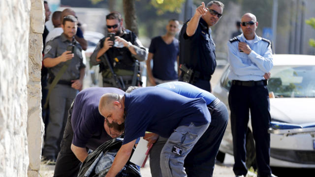 An Israeli police officer, center front, checks the dead body of a Palestinian man who was shot dead after authorities say he drew a knife and tried to stab the officers who shot him in a street in Jerusalem Oct. 17, 2015. 