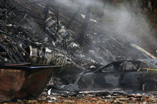A charred car and aircraft debris smolder where authorities say a small business jet crashed into an apartment building in Akron, Ohio, Nov. 10, 2015. 