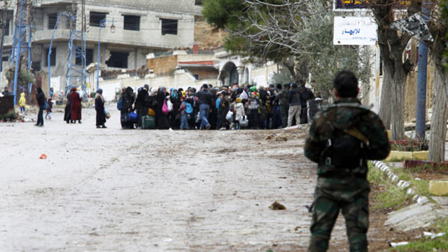 Syrian army soldiers monitor residents who said they have received permission from the Syrian government to leave Madaya, Syria, as they wait with their belongings after an aid convoy entered the besieged town Jan. 14, 2016. 