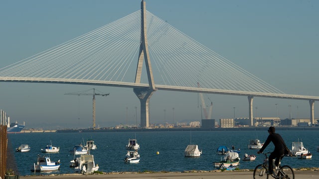 A fisherman cycles towards his boat with the landmark 1812 Consttiution Bridge in the background 