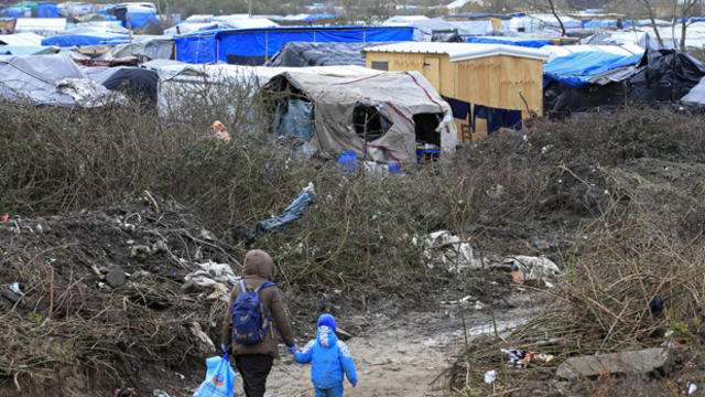 ​A migrant and her child walk in the southern part of a camp for migrants called the "jungle" in Calais, France, Feb. 25, 2016. 