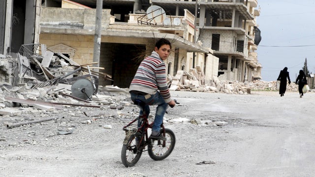 A boy rides a bicycle near damage in Kafr Hamra village, northern Aleppo countryside, Syria, Feb. 27, 2016. 