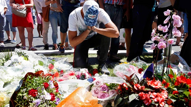 A man reacts near bouquets of flowers as people pay tribute near the scene where a truck ran into a crowd at high speed, killing scores and injuring more who were celebrating the Bastille Day national holiday, in Nice, France, July 15, 2016.​ 