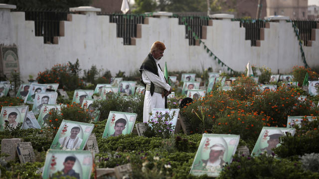 A Yemeni man offers prayers at the portrait adorned grave of his relative who was killed in the ongoing conflict in Yemen, at cemetery in Sanaa 