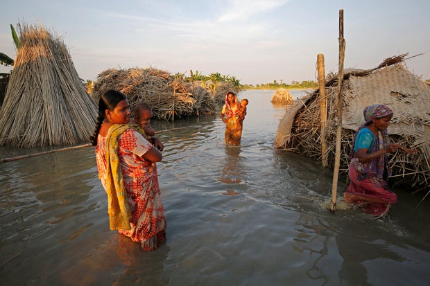 Women carry children as they make their way through a flooded area in Bogra