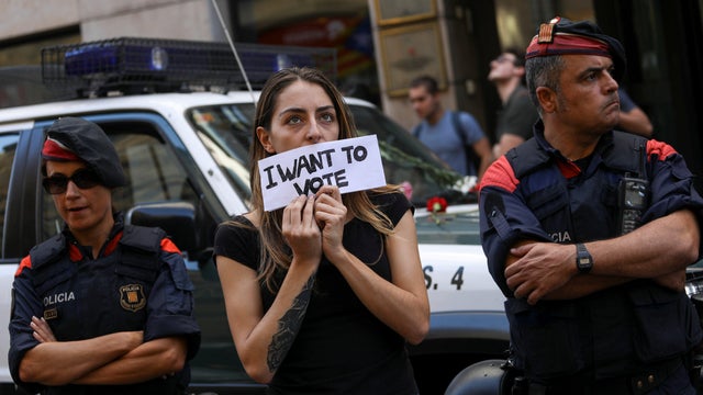 A protestor holds up a sign in front of a Catalan police outside the Catalan region's foreign affairs ministry building during a raid by Spanish police on government offices, in Barcelona 