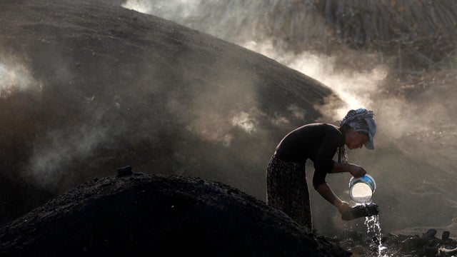 A woman sprays water on burning woods during a charcoal making process near Kizilcahamam 