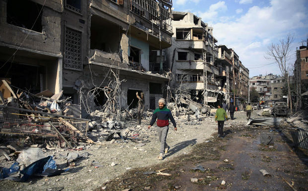 People walk through air raid damage in the besieged town of Douma, Eastern Ghouta, Damascus 