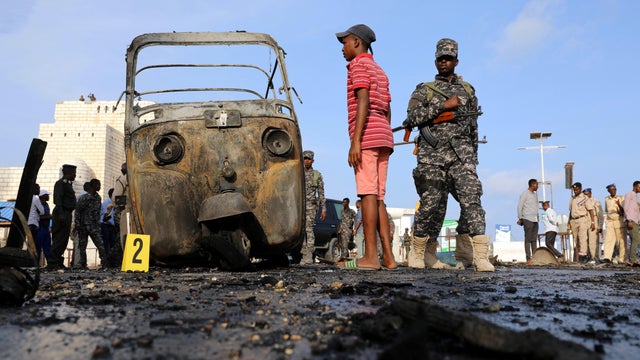 A Somali military officer and residents look at the scene of an explosion at a checkpoint near Somalia's parliament and interior ministry in Mogadishu 