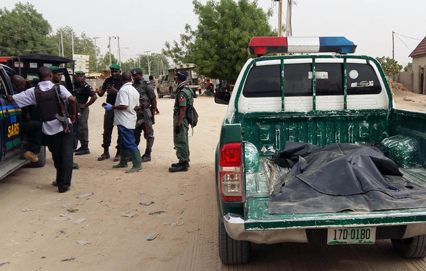 A covered-up dead body lies in the trunk of a police vehicle as members of security forces stand near the site of a suspected Boko Haram attack on the edge of Maiduguri's inner city 