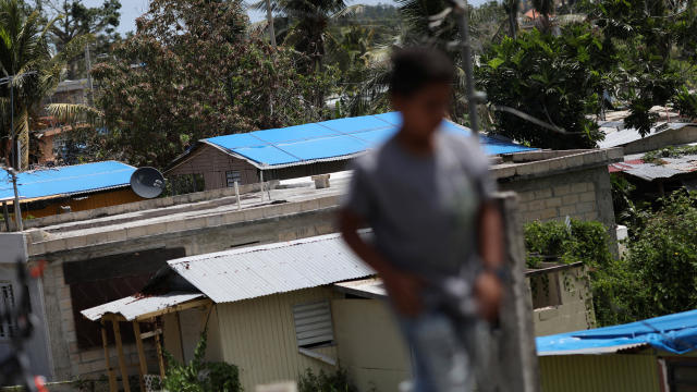 A boy walks near houses with plastic sheets replacing roofs hit by Hurricane Maria in September, in a neighborhood in Canovanas, Puerto Rico, April 10, 2018. 