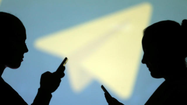 Silhouettes of mobile users are seen next to a screen projection of the Telegram logo in this picture illustration taken March 28, 2018. 