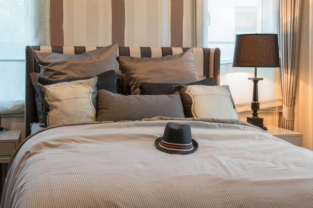cozy bedroom interior with dark brown pillows and black hat on bed 